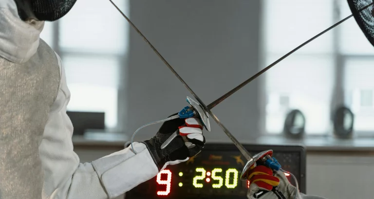 Two fencers crossing weapons in front of a score box