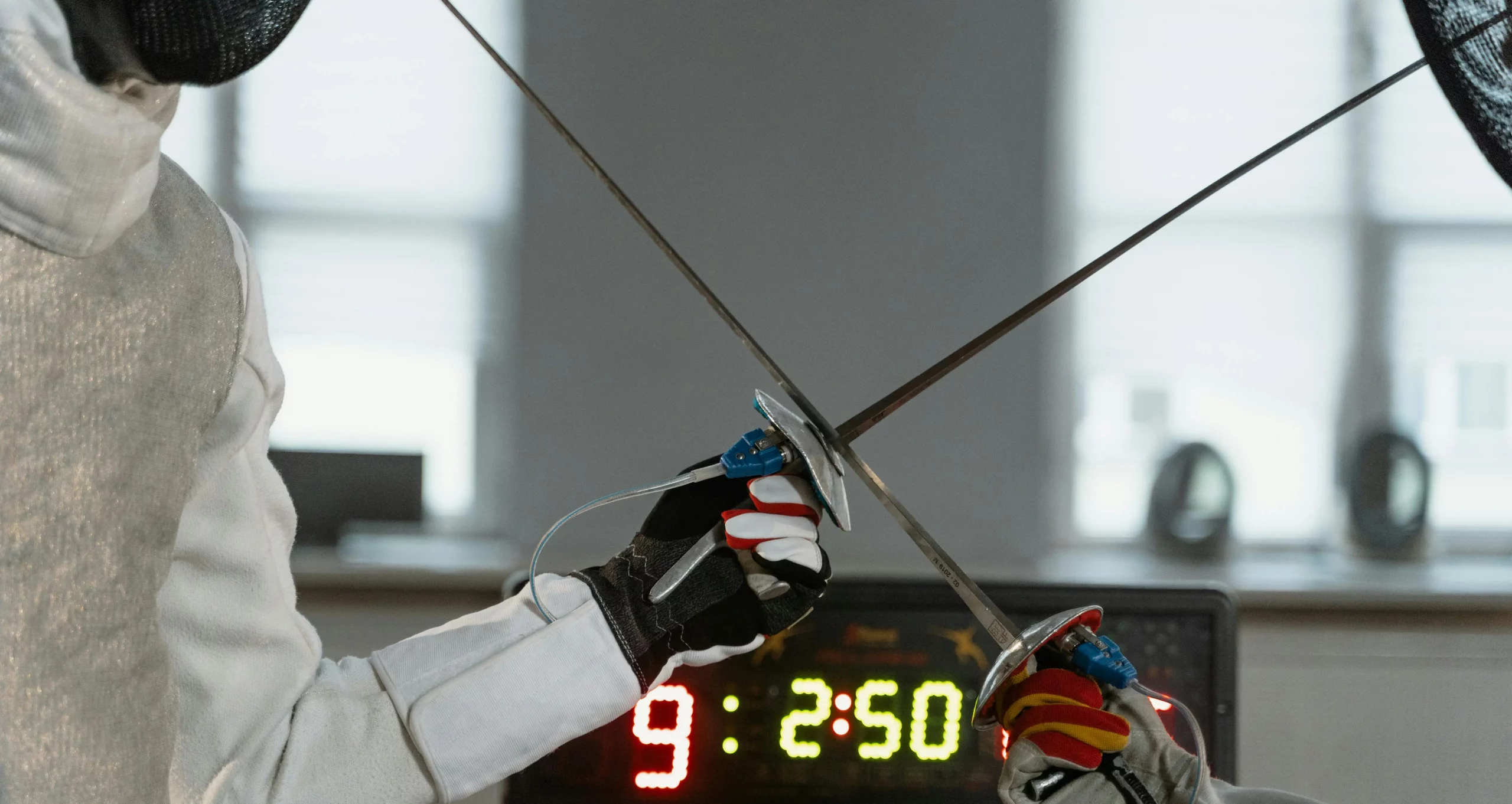 Two fencers crossing weapons in front of a score box